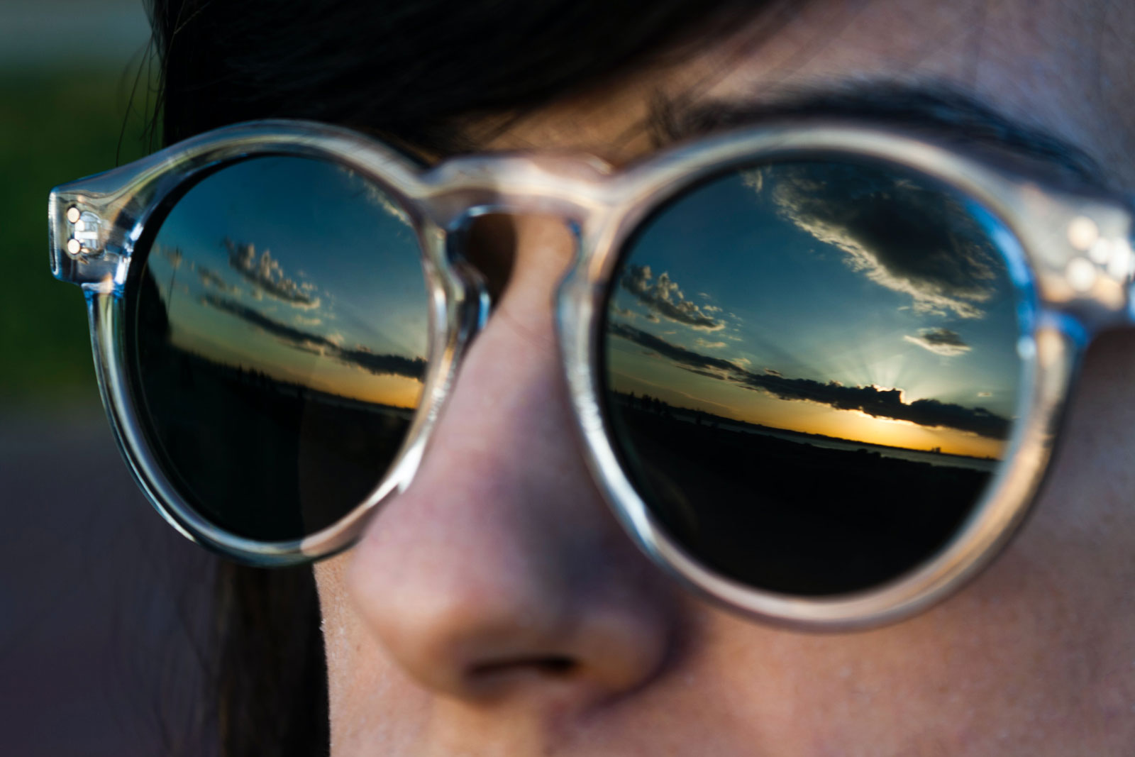 Jemand trägt eine Sonnenbrille, in der sich die Wolken spiegeln