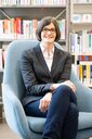 Lucia Werder sitzt auf einem Sessel vor einem Bücherregal.