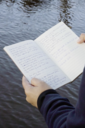 Man sieht ein Notizbuch, in dem ein handgeschriebenes Gedicht steht, im Hintergrund Wasser.